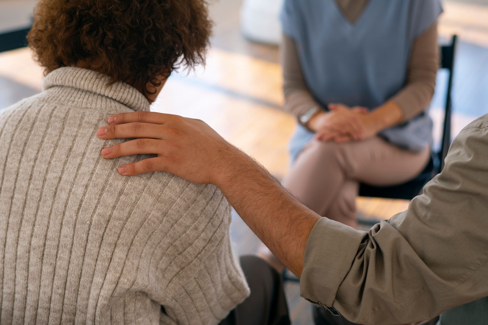 Person rests a hand on another’s shoulder during a seated support group meeting