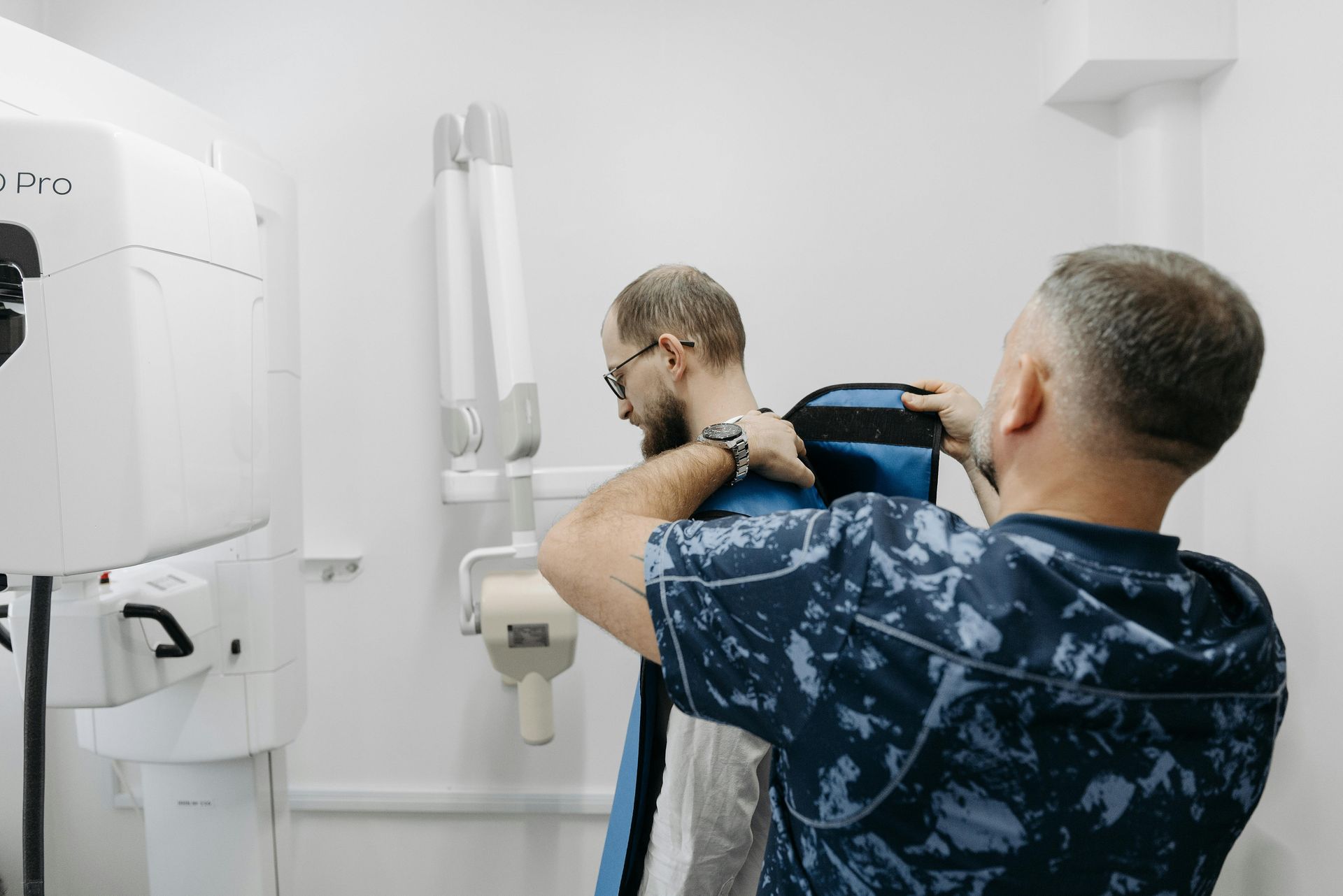 Two technicians adjust a person’s shoulder in a bright medical imaging room.