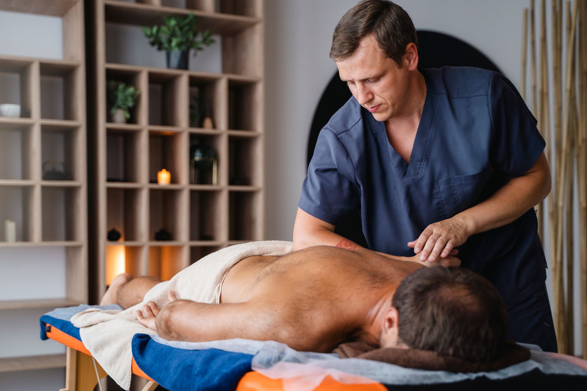 Massage therapist working on a client’s back in a calming spa room with shelves and candles