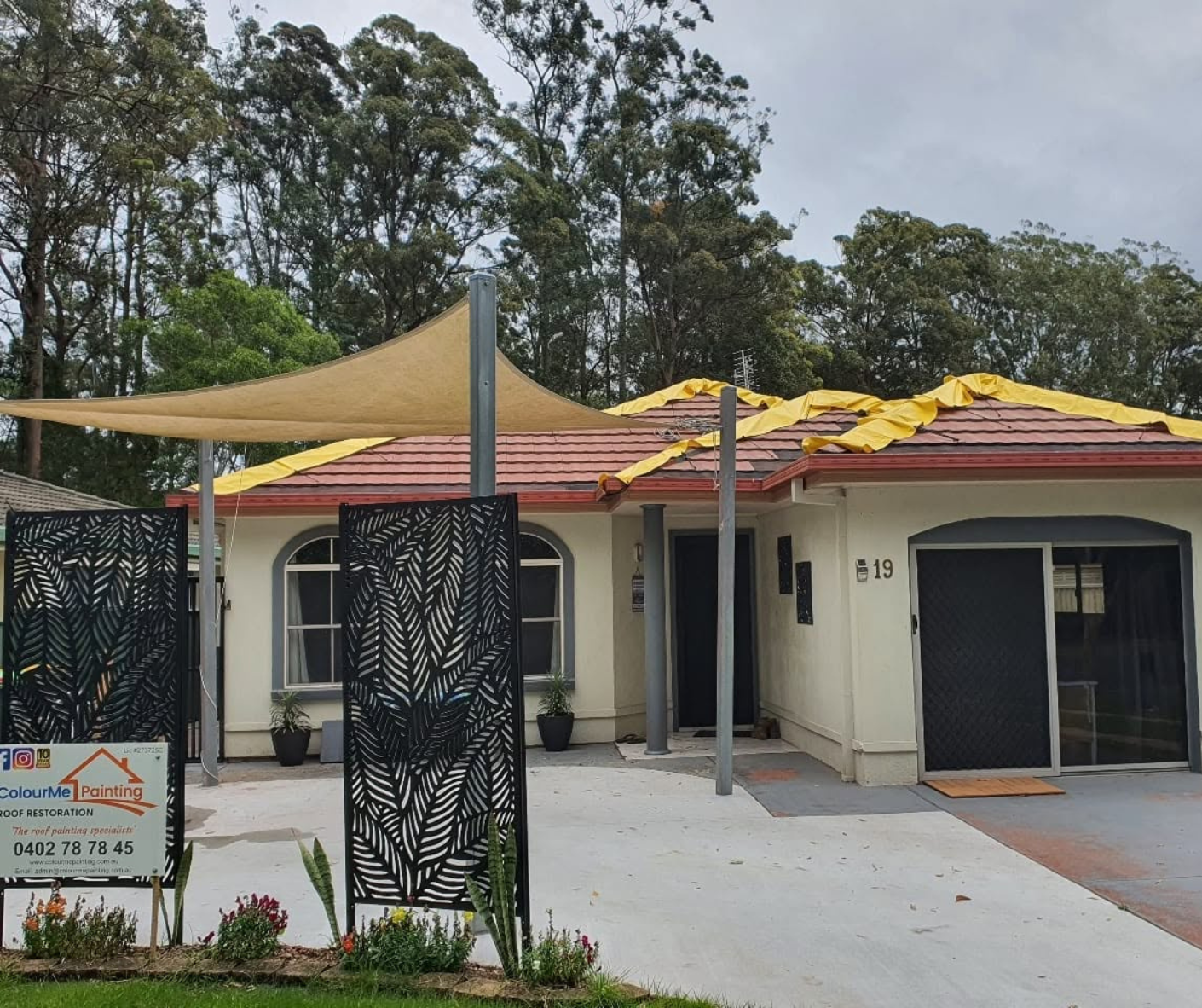 Single-story cream house with red-tiled roof, black gate, and beige shade sails over the front driveway.