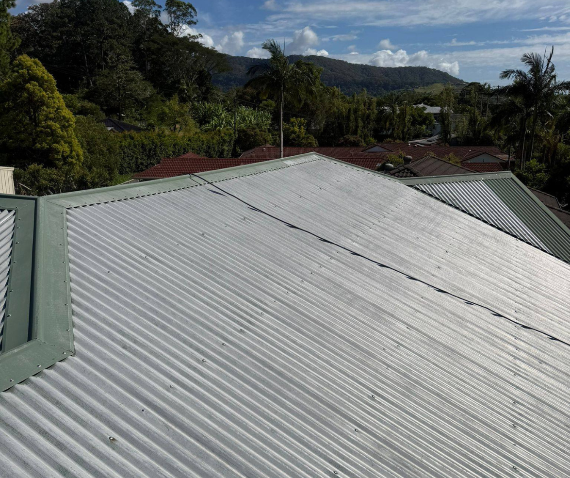 Corrugated metal roof in the foreground with green trees and distant hills under a cloudy sky Corrugated metal roof in the foreground with green trees and distant hills under a cloudy sky