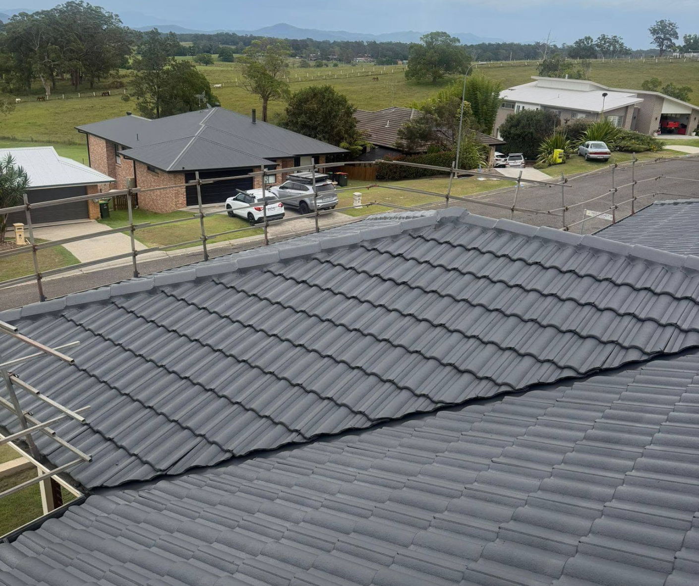 Grey tiled rooftops in a suburban neighborhood under a clear sky, with trees and houses in the background Grey tiled rooftops in a suburban neighborhood under a clear sky, with trees and houses in the background