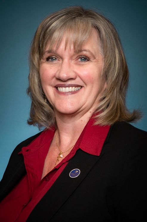 A woman in a red shirt and black jacket is smiling for the camera.