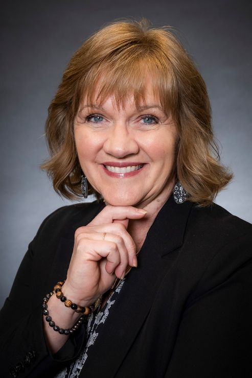 A woman in a red shirt and black jacket is smiling for the camera.