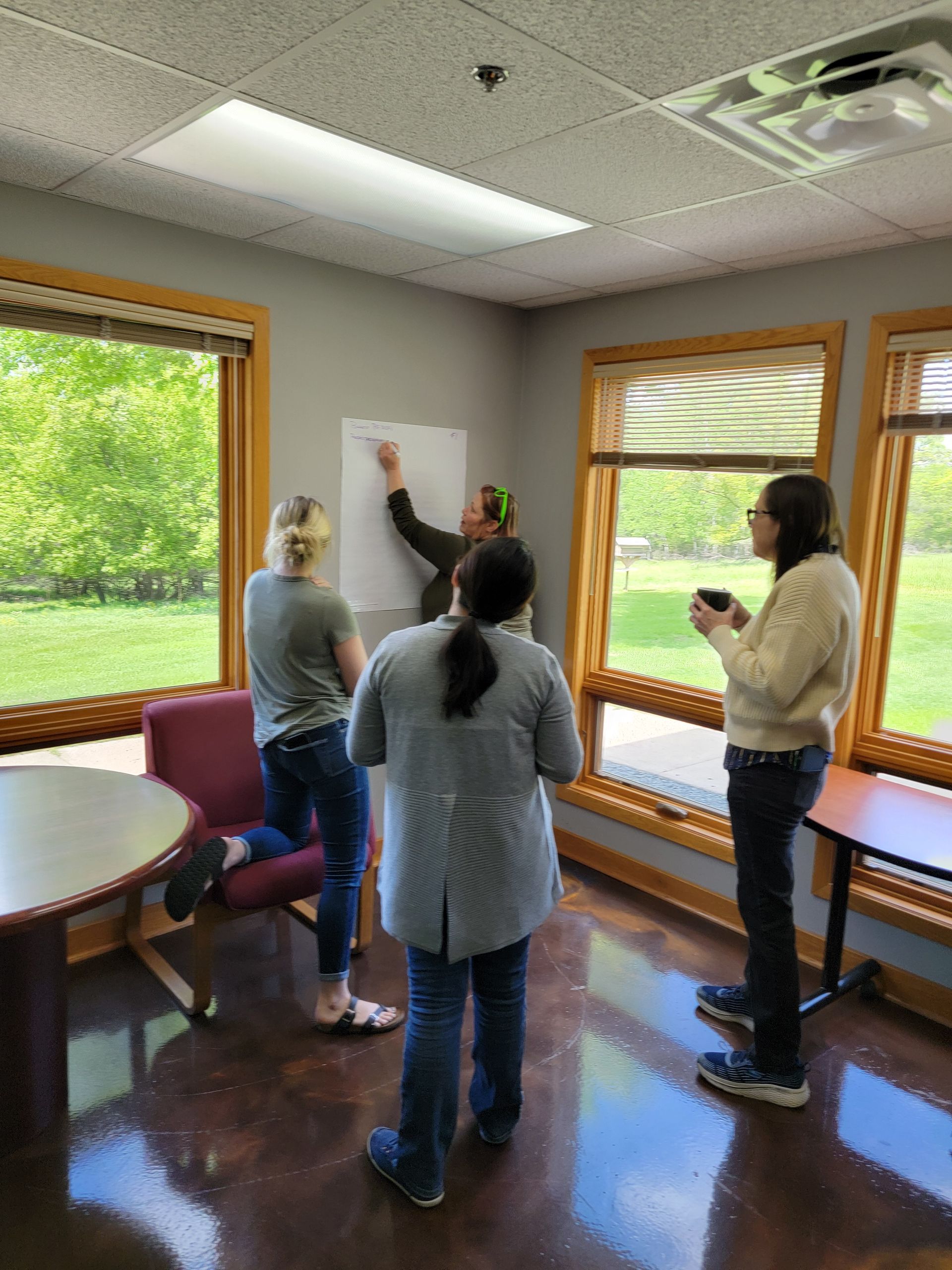 A group of people are standing in a room in front of a window.