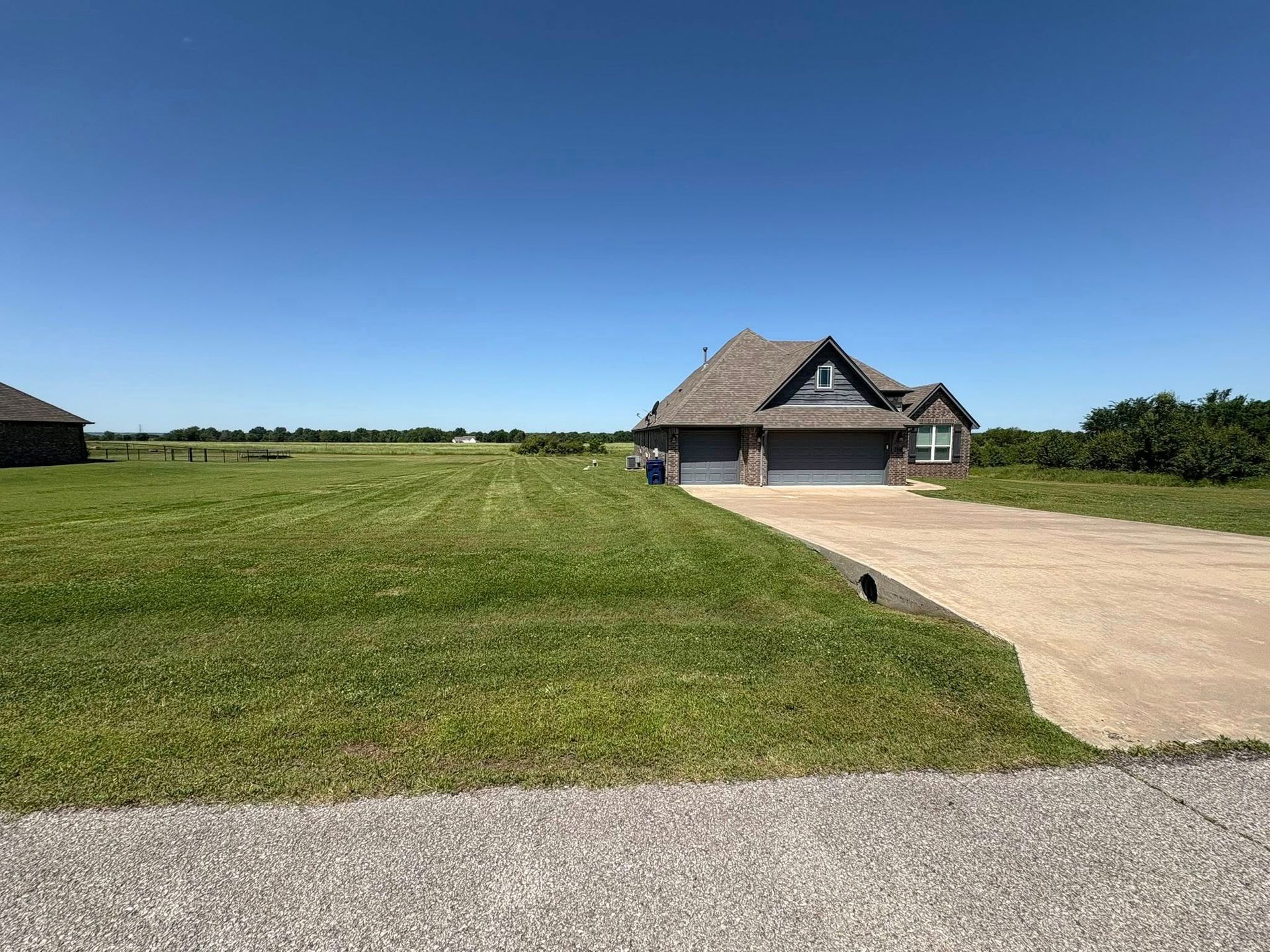 House with a gray roof and attached garage, set on a large grassy lot under a blue sky.