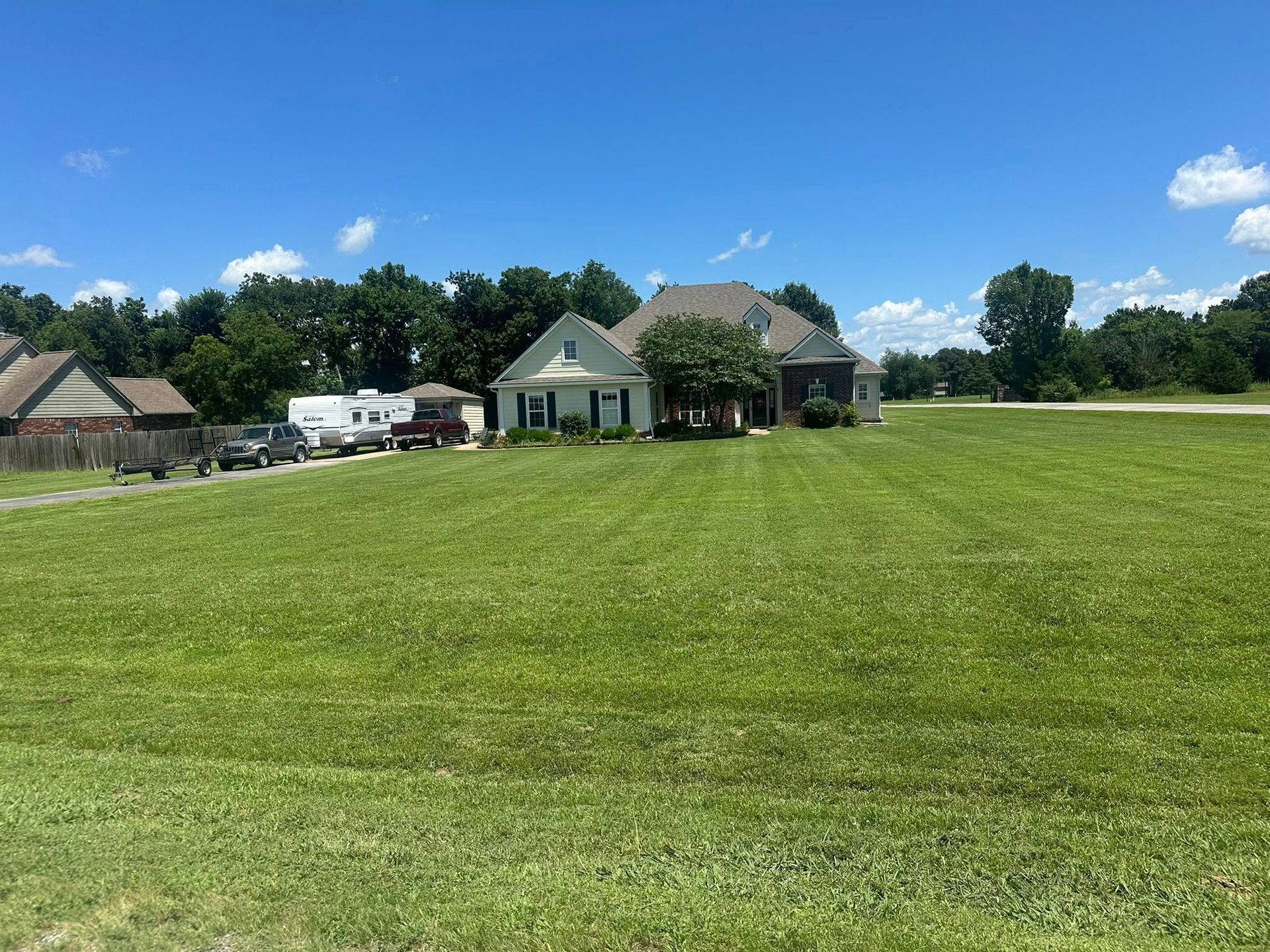Green lawn with two houses and trees under a blue sky.