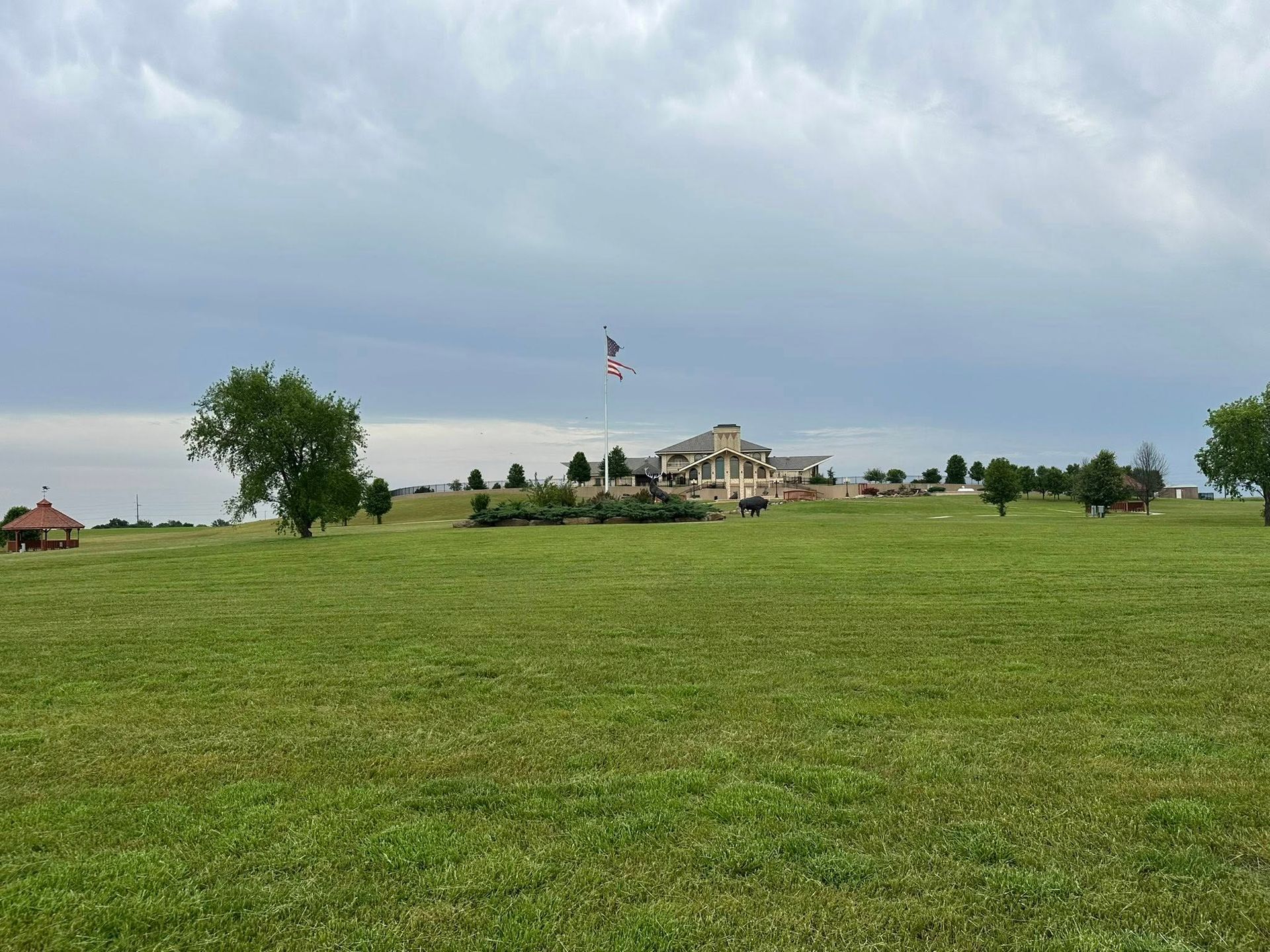 A large, light-colored building with a flag on a grassy hill under an overcast sky.
