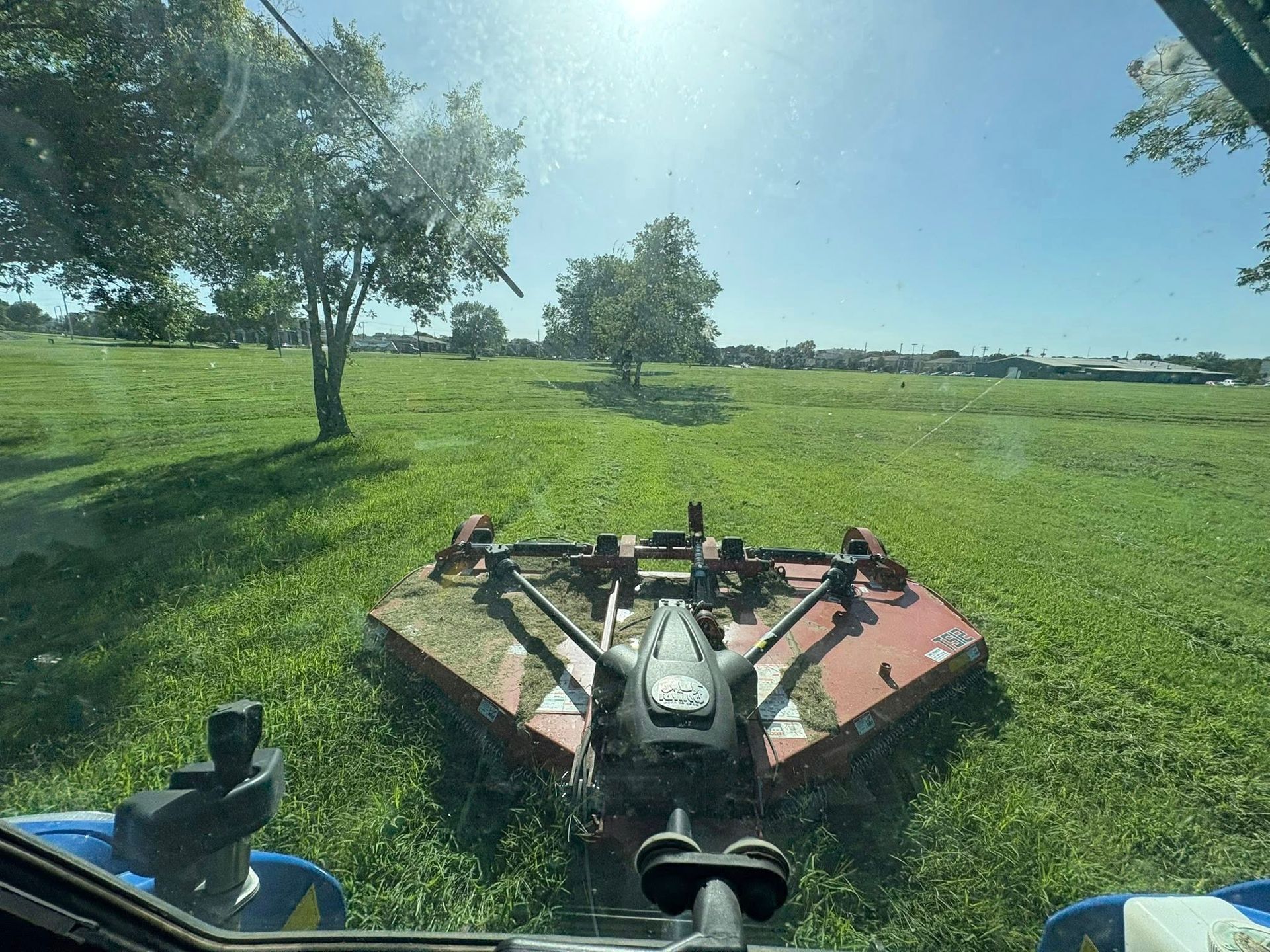 View from a tractor cab mowing a grassy field under a bright blue sky.