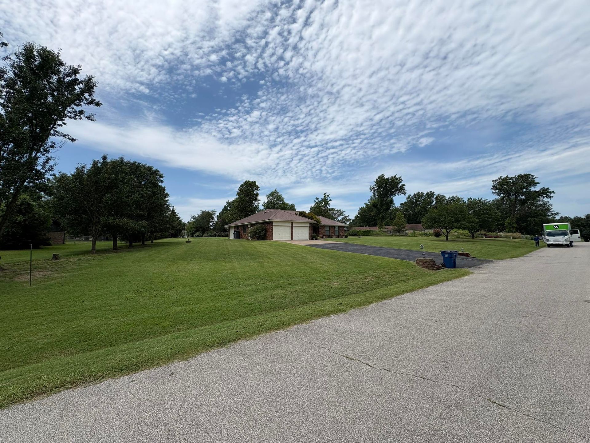 House with brown roof and two-car garage on a grassy lot, under a blue sky with streaky clouds.