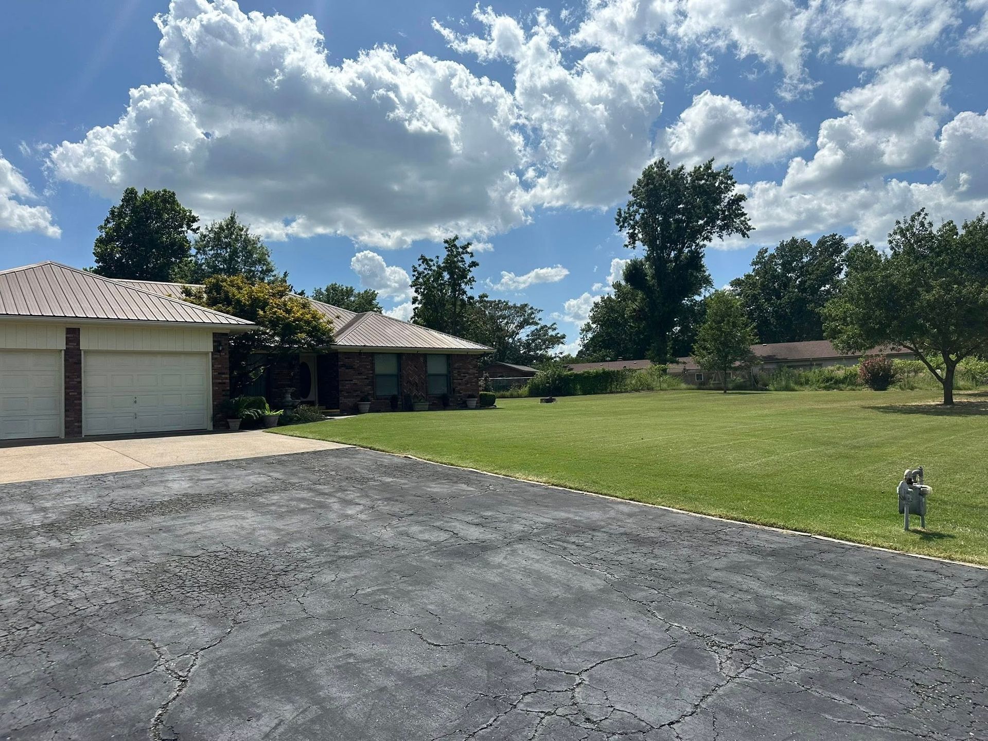 House with brick facade, lawn, and blue sky with clouds. Asphalt driveway and small dog visible.