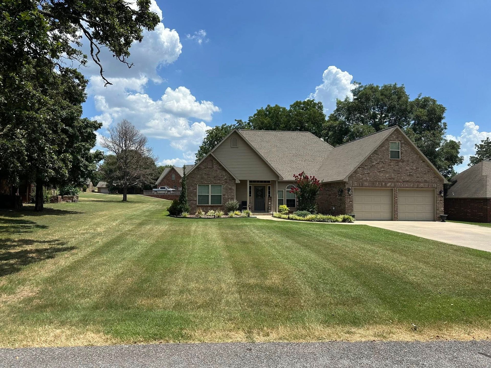 Brick house with a two-car garage, manicured lawn, and blue sky.