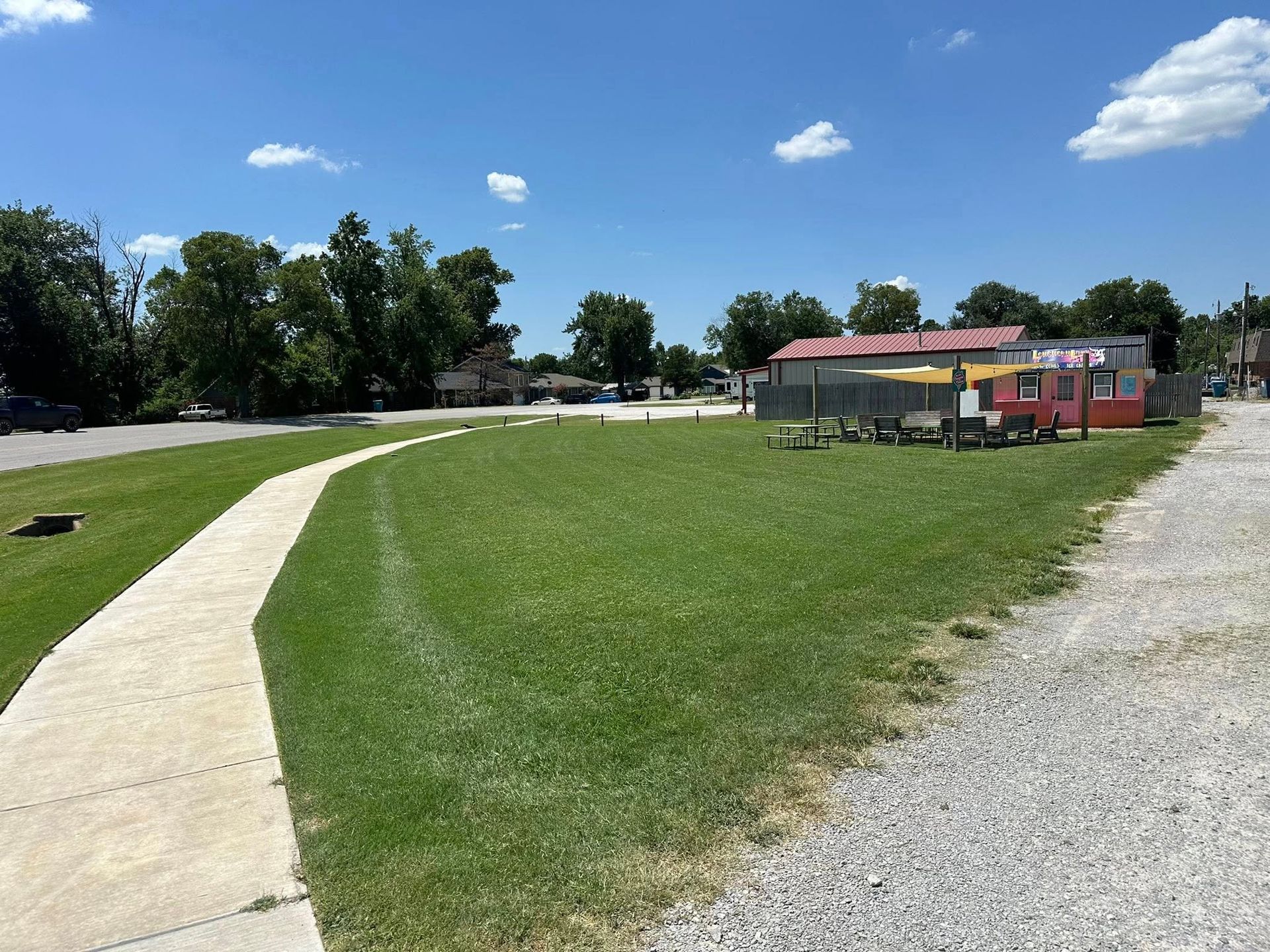 A sunny day view of a grassy field with a sidewalk and a colorful building.