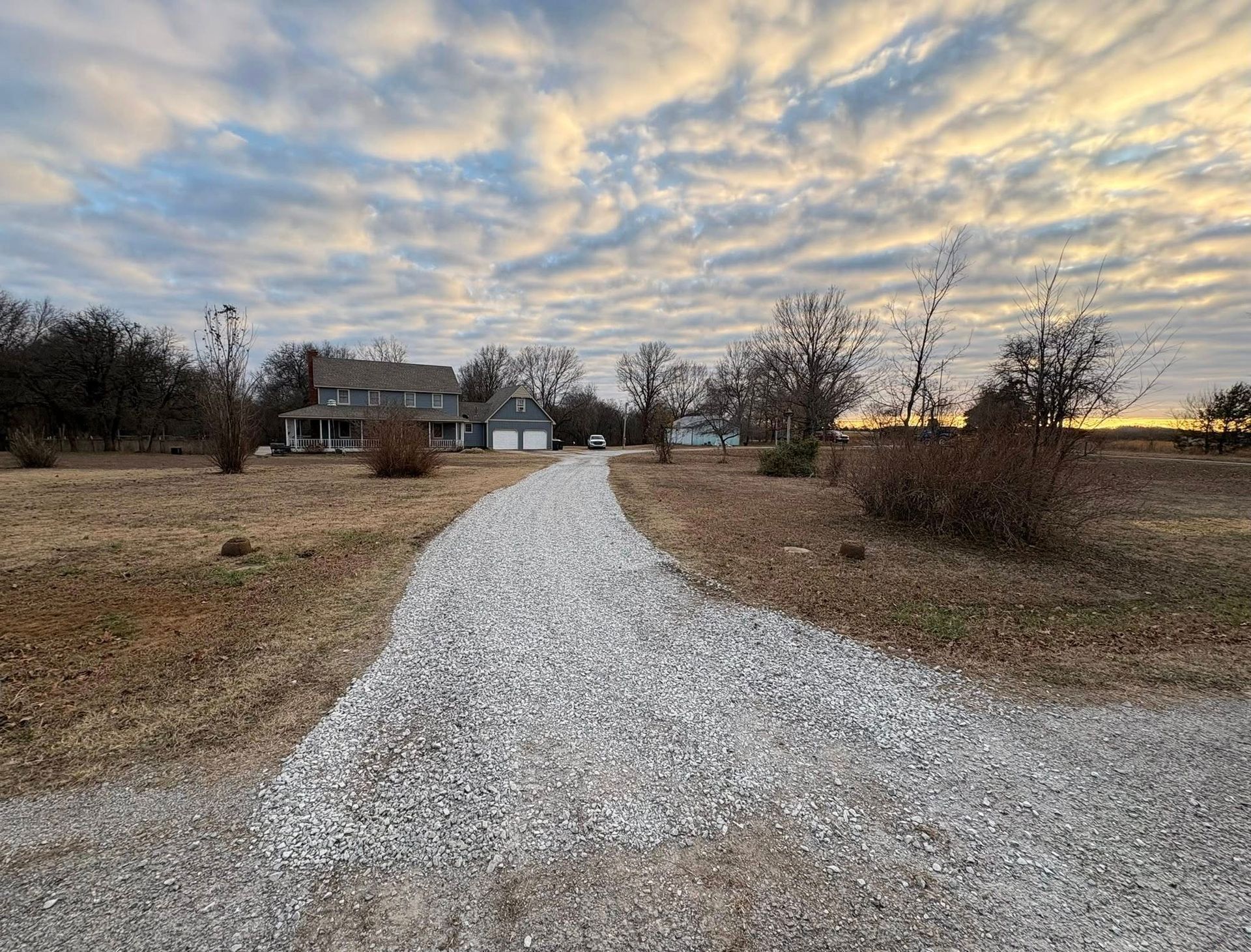 Gravel driveway leading to a two-story house with a garage, under a cloudy sky.