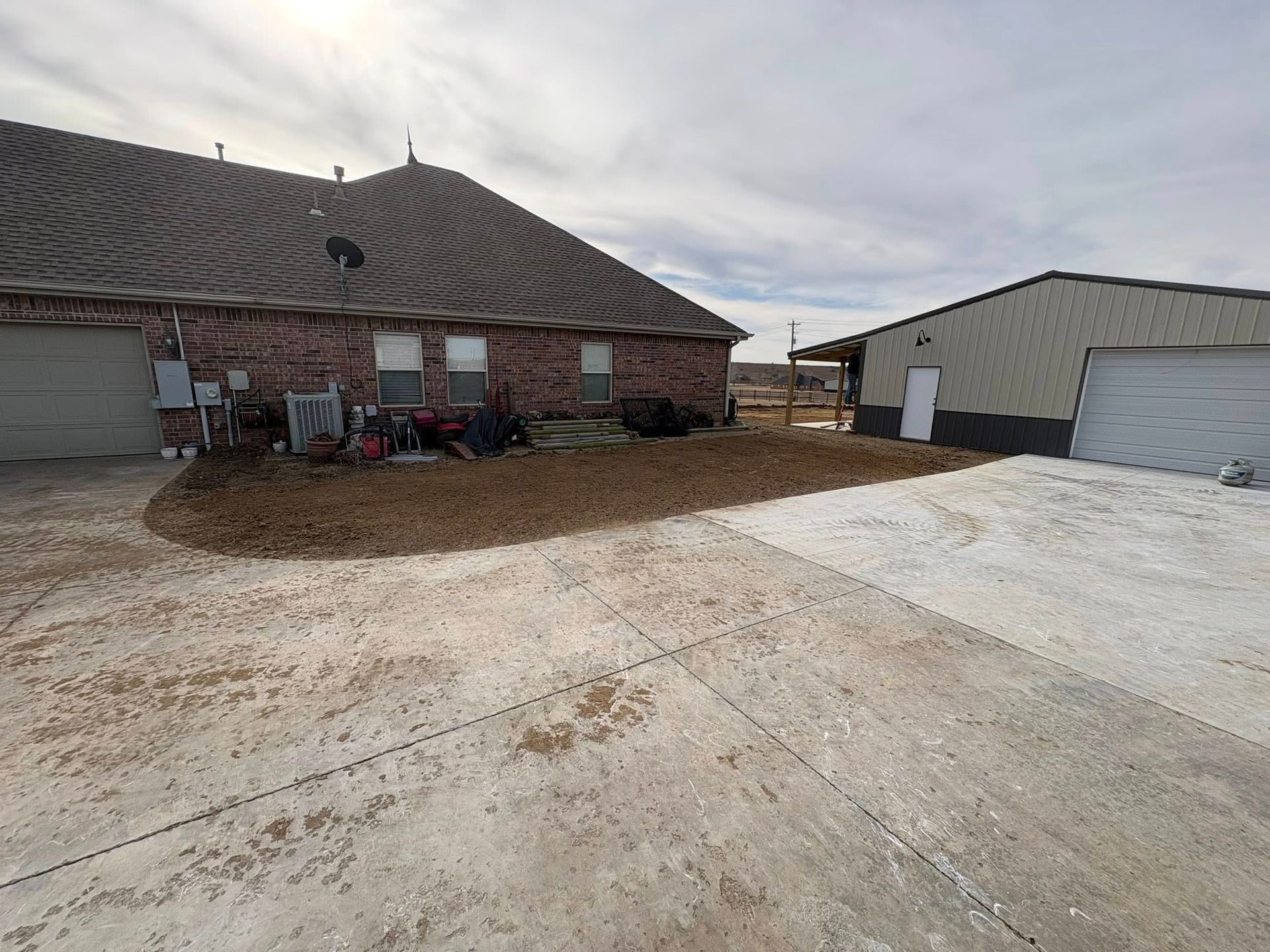 A house with a dirt patch and garage on a concrete driveway under a cloudy sky.