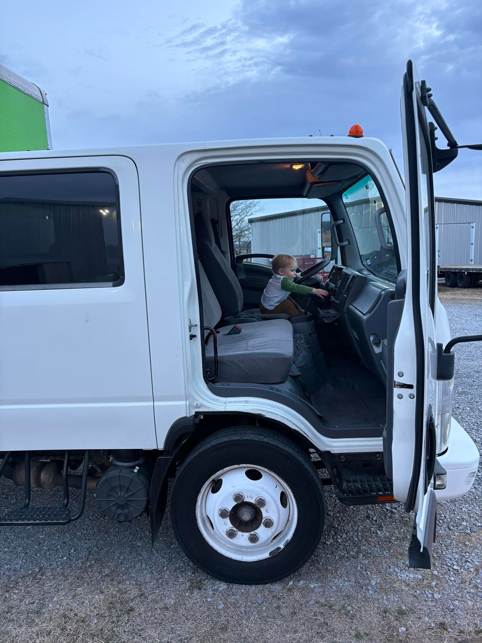 White Isuzu truck with open door, driver's seat visible, parked outdoors.