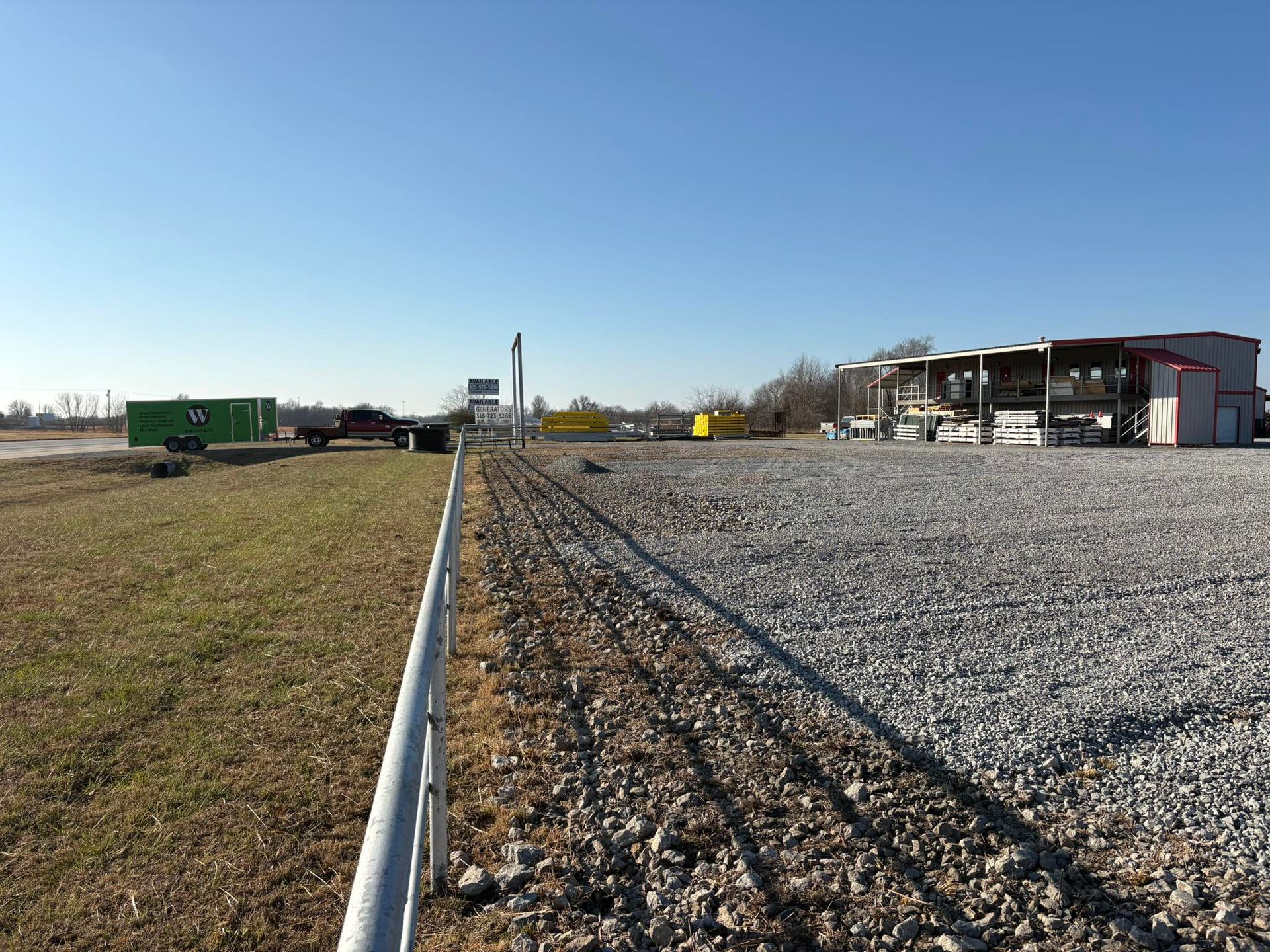 Gravel-covered lot with industrial equipment and trailers under a clear blue sky.