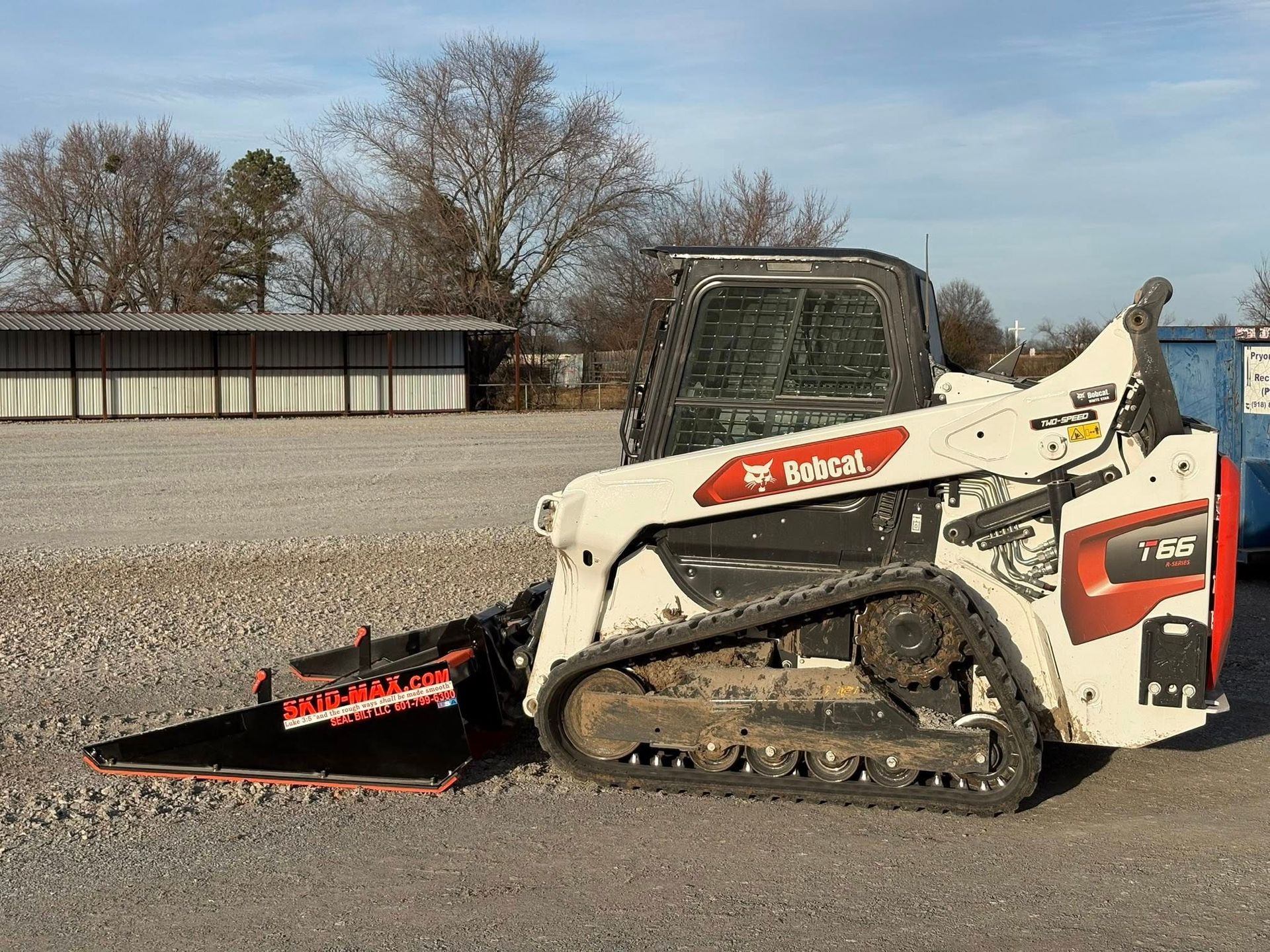 Bobcat skid-steer loader with a blade attachment grading gravel in an outdoor setting.