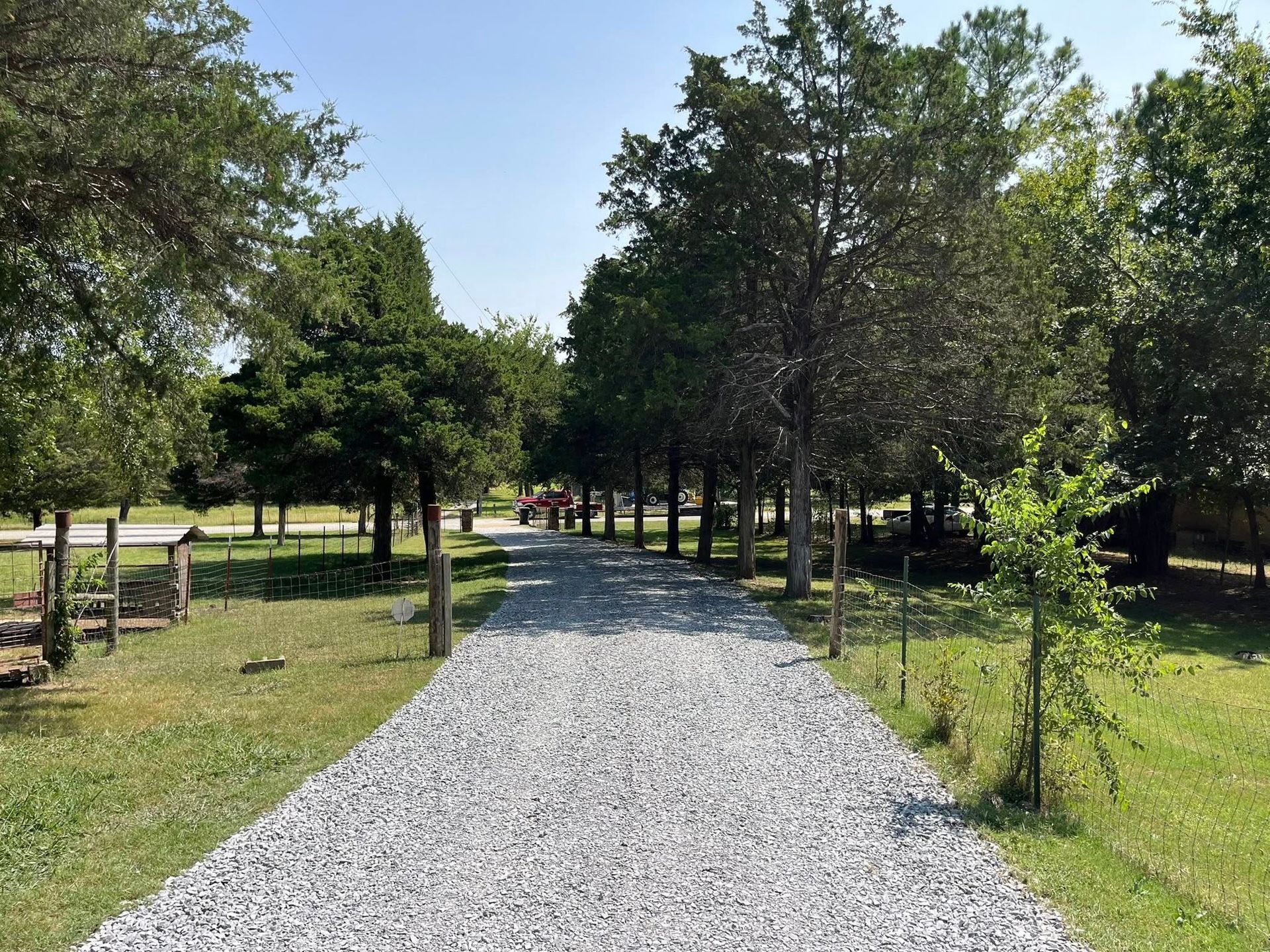 Gravel pathway through a park with trees on both sides and a glimpse of people in the distance on a sunny day.