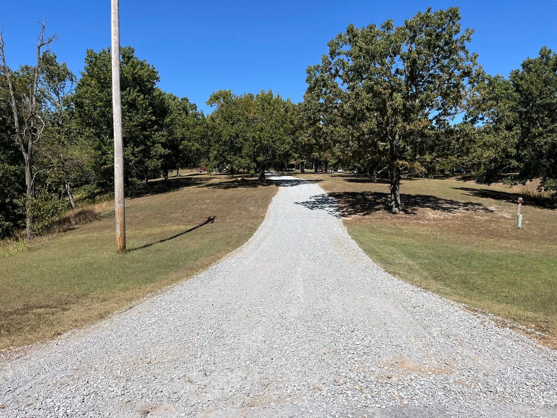 Gravel driveway leading through grassy area with trees, under a blue sky.