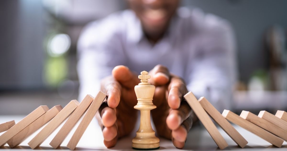Person protecting a chess king from falling dominoes.