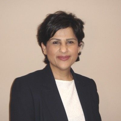 Portrait of a person in a dark blazer and white top against a plain beige background.
