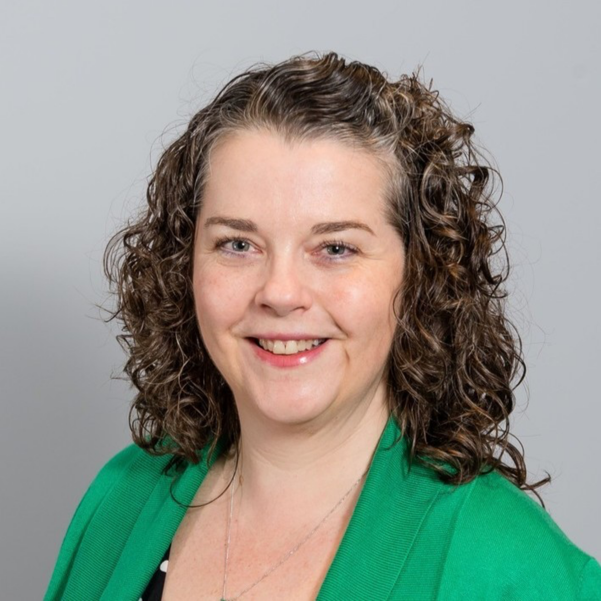 Smiling woman with curly hair wearing a green top against a gray background - nicola asthma