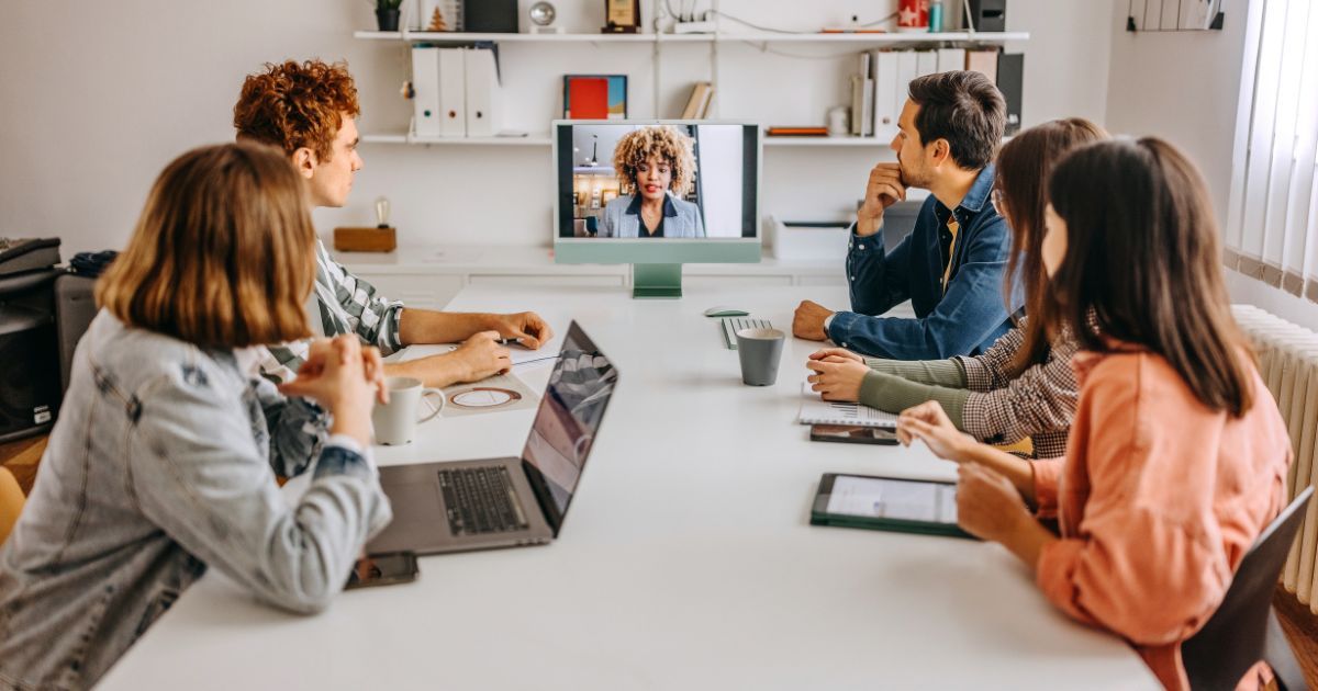 People in office meeting with person on screen via video call.