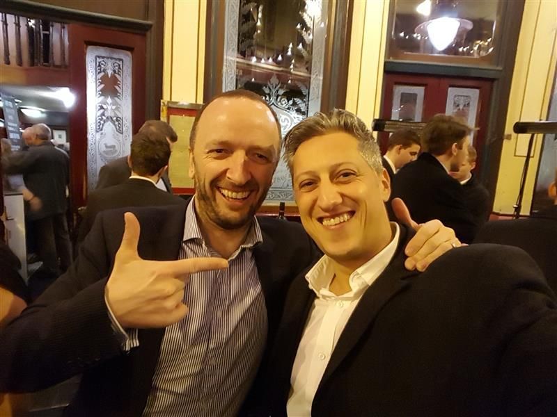 2 men in suits smiling as one points to the other