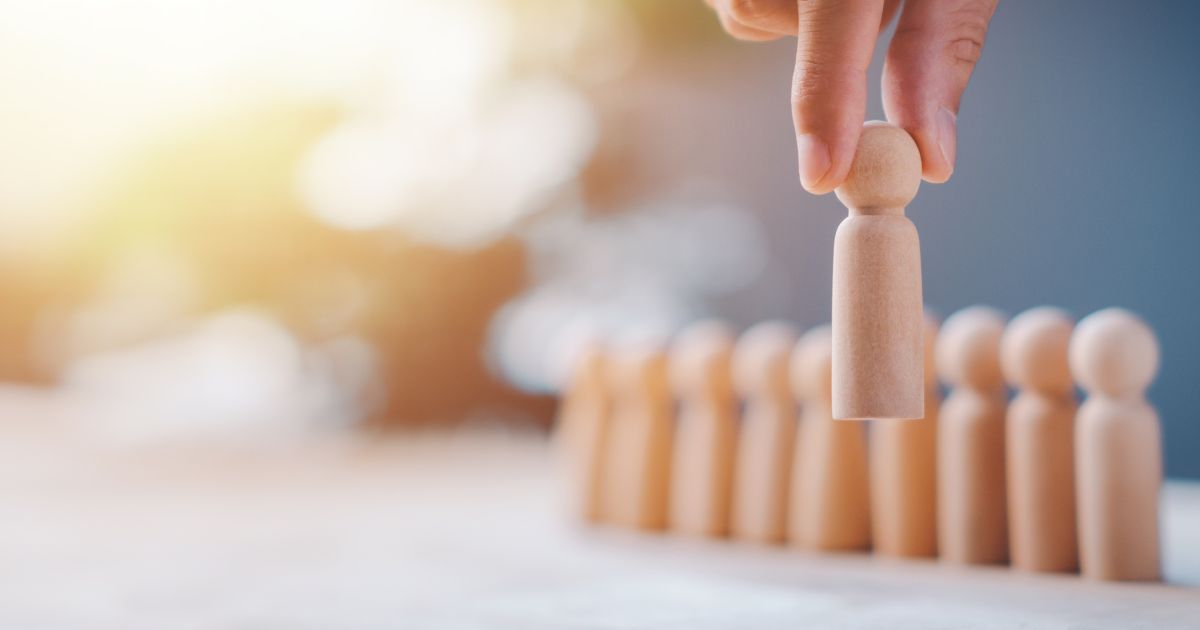 Hand placing a wooden figure in a row of similar figures, symbolizing selection or leadership.