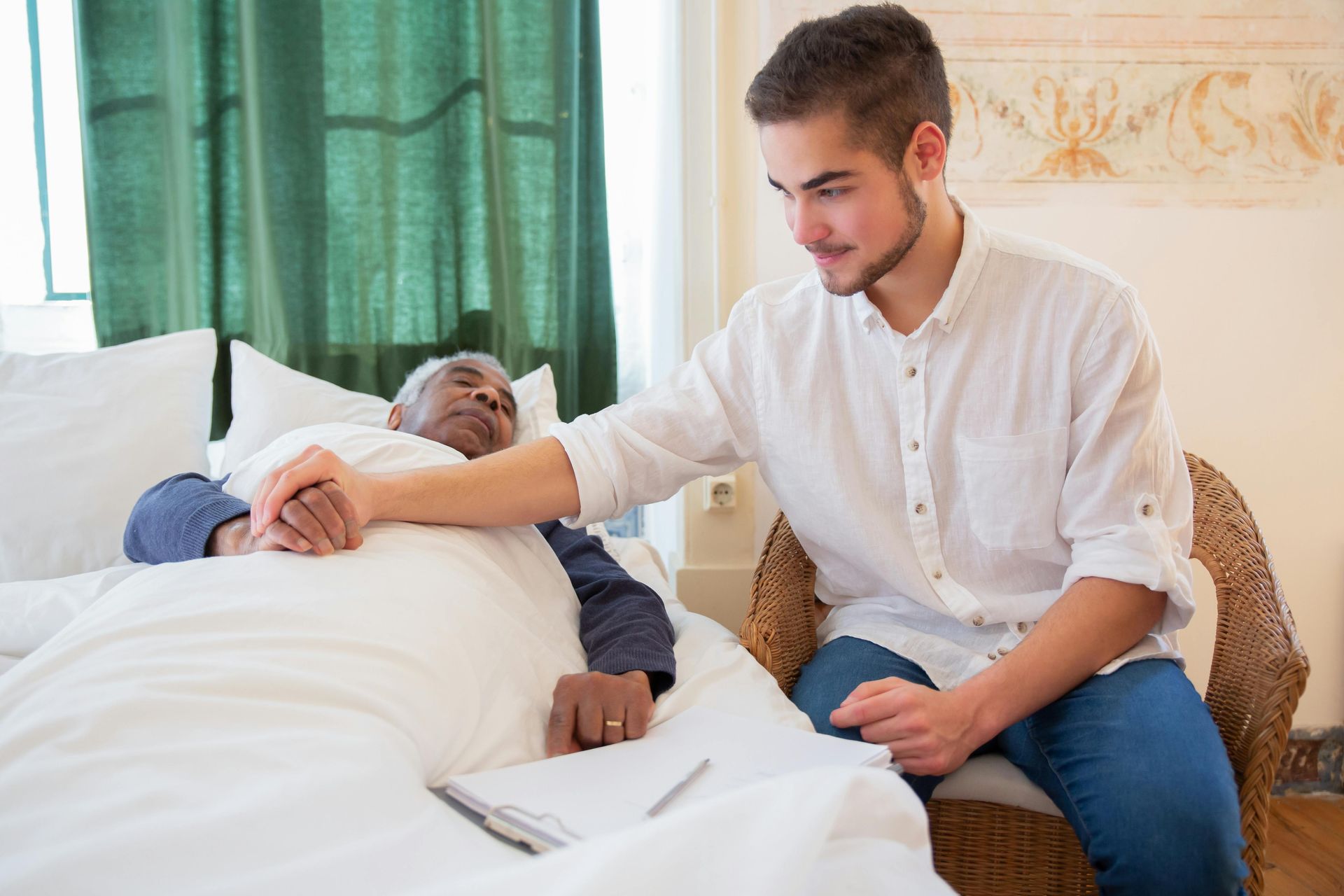 A young man is sitting next to an elderly man laying in a bed.