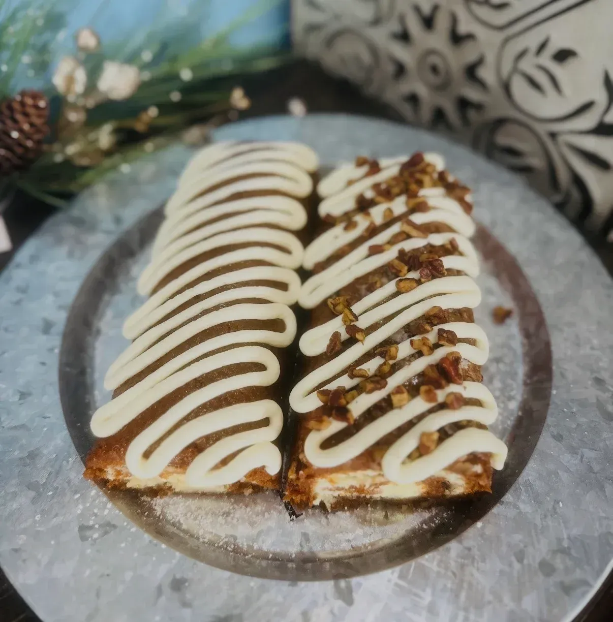 Two rectangular pastries drizzled with white icing, one with pecans, on a silver plate.