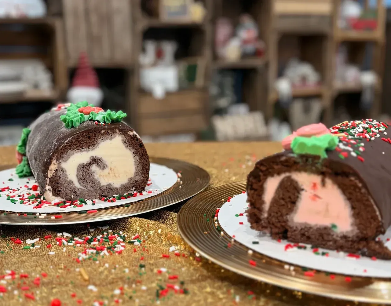 Two chocolate yule logs with cream filling and festive decorations on gold plates, sprinkled with colorful confetti.