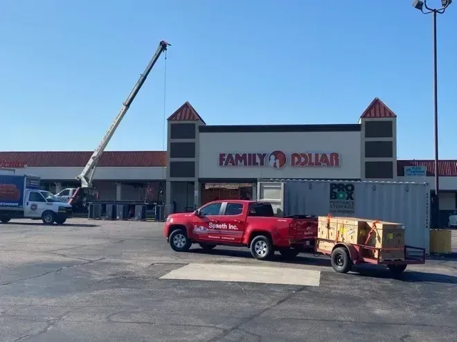 A Family Dollar store being worked on with a crane, truck, and trailer. Red truck and trailer in the front.