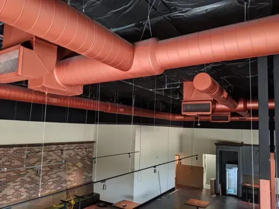 Copper-colored HVAC ducts run across a black ceiling in an unfinished commercial space.