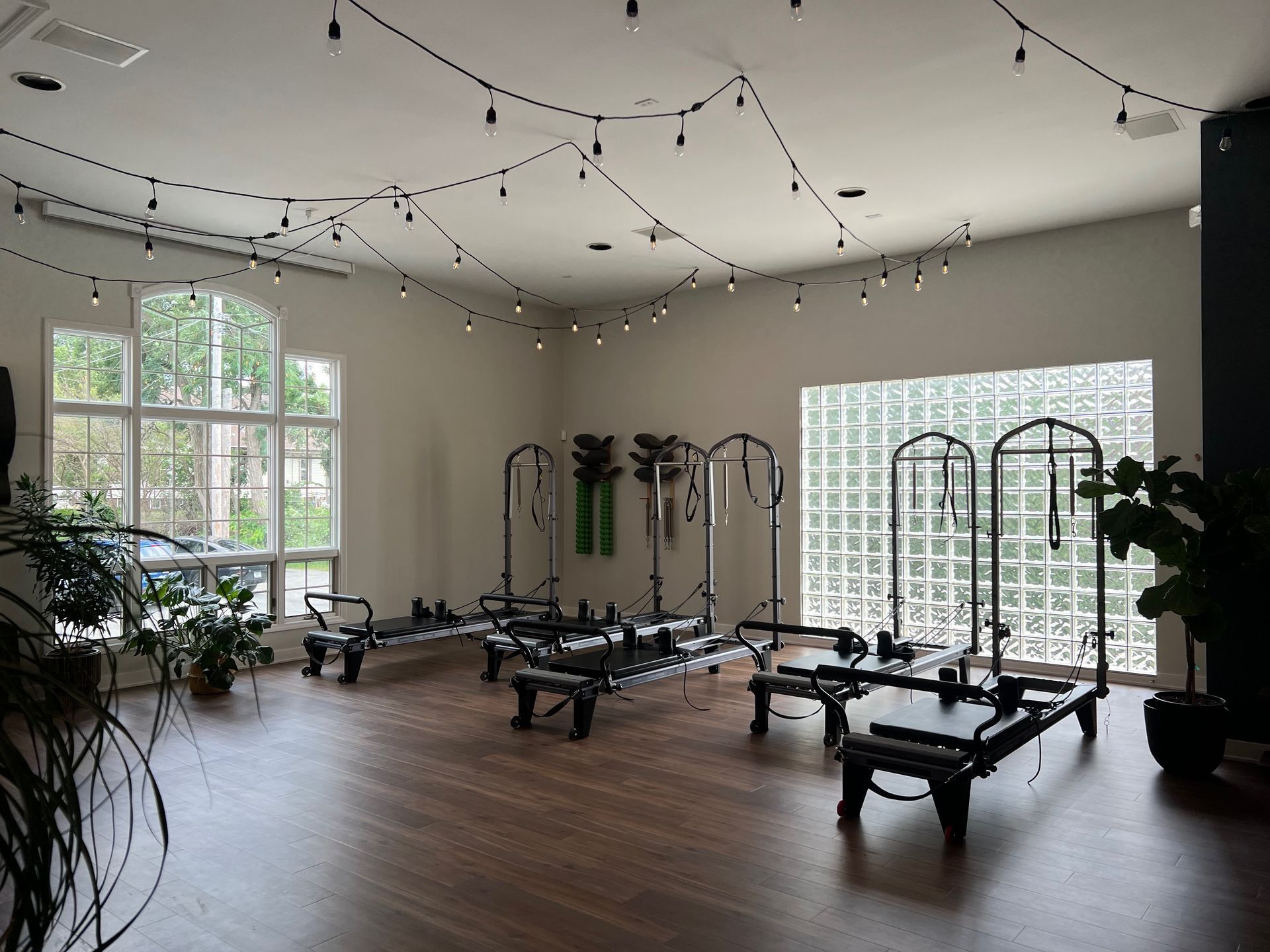 A beautiful room with pilates reformers and other exercise equipment. The room has large windows and string lights.