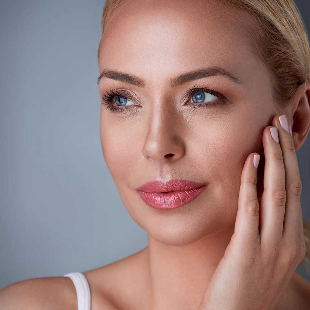 a woman with blue eyes is touching her face with her hand.
