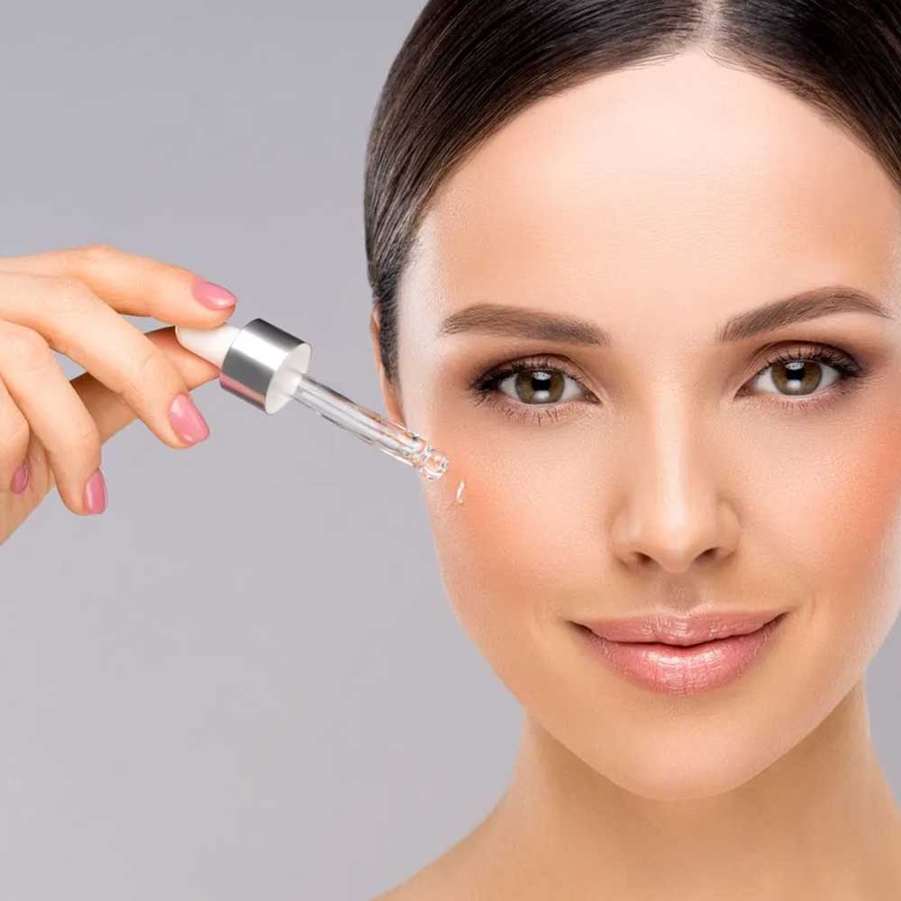 a woman is applying a serum to her face with a pipette