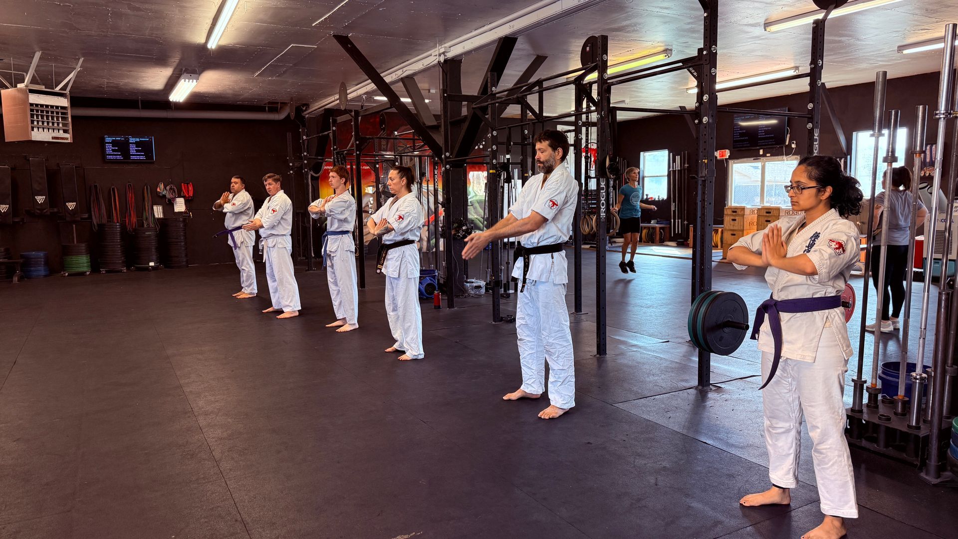 Two men in karate uniforms with black belts are standing next to each other in a gym.