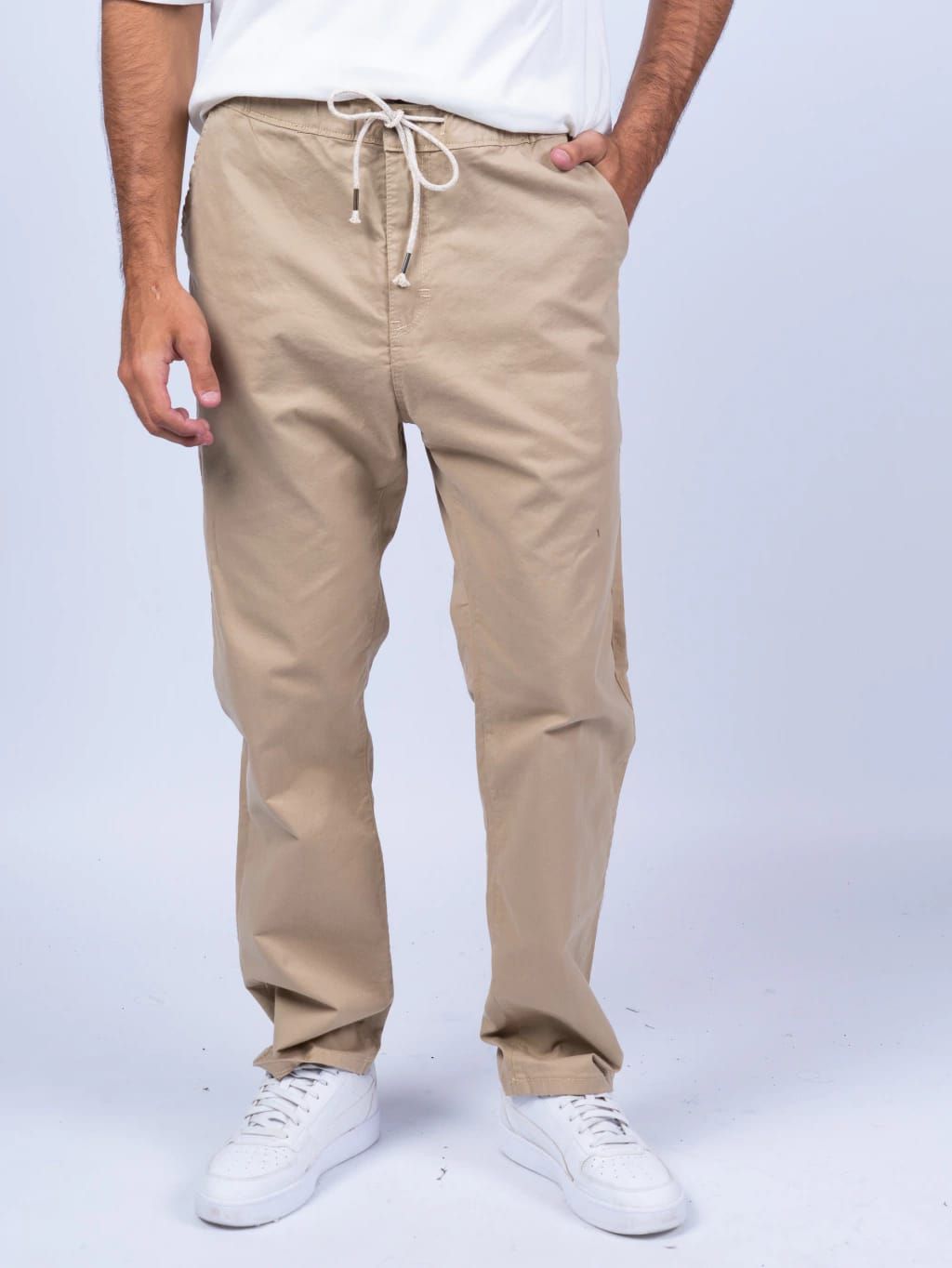 Hombre que lleva pantalones color canela con zapatos blancos, cintura con cordón y manos en los bolsillos.