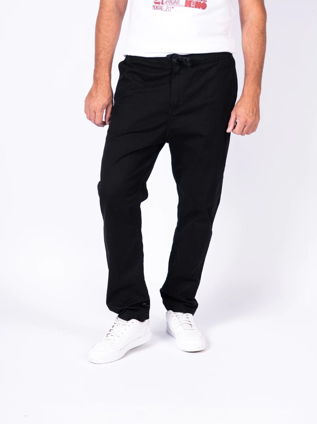 Hombre que lleva pantalones color canela con zapatos blancos, cintura con cordón y manos en los bolsillos.