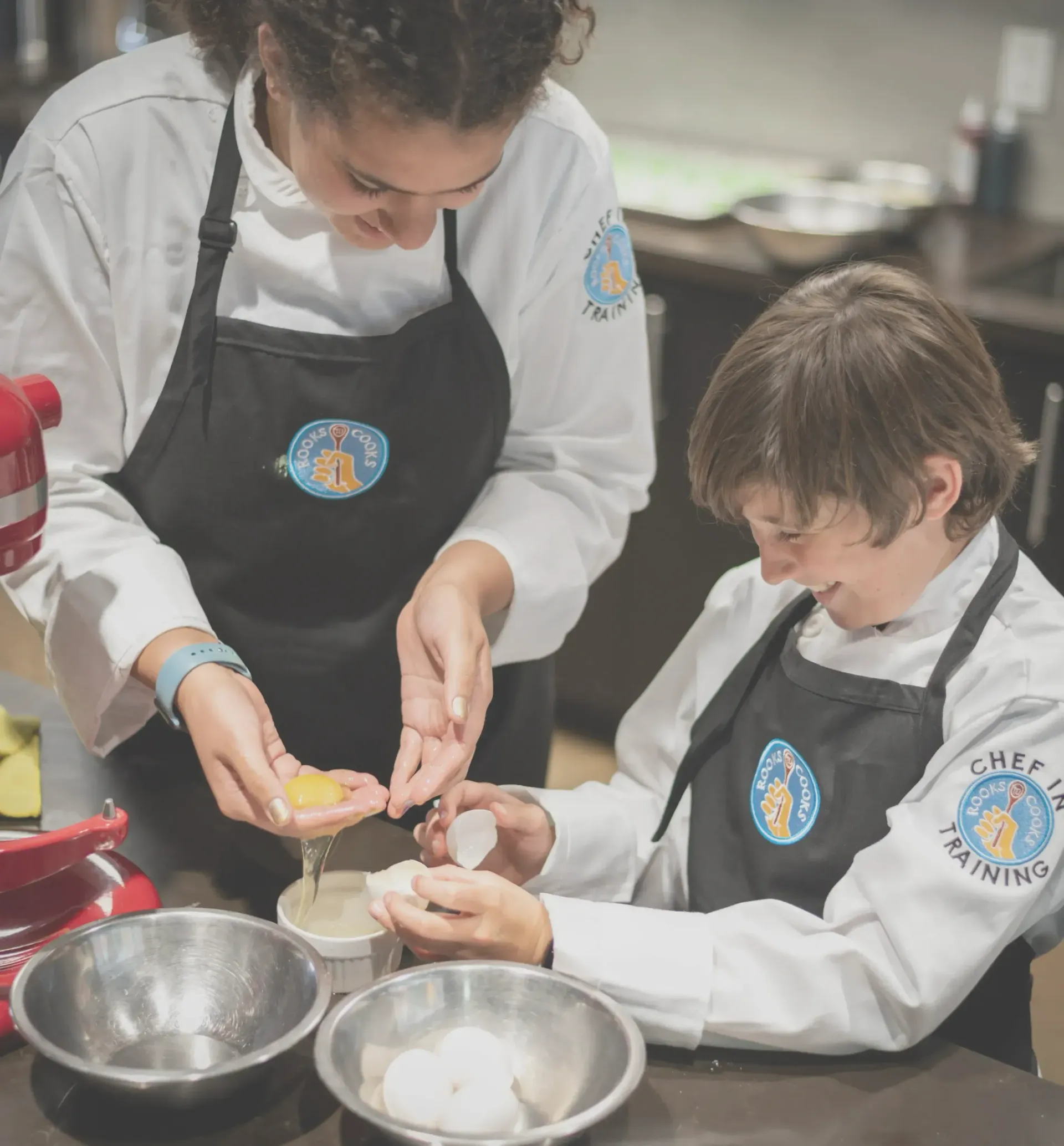 A cooking counsellor and camper smiling as they separate eggs.