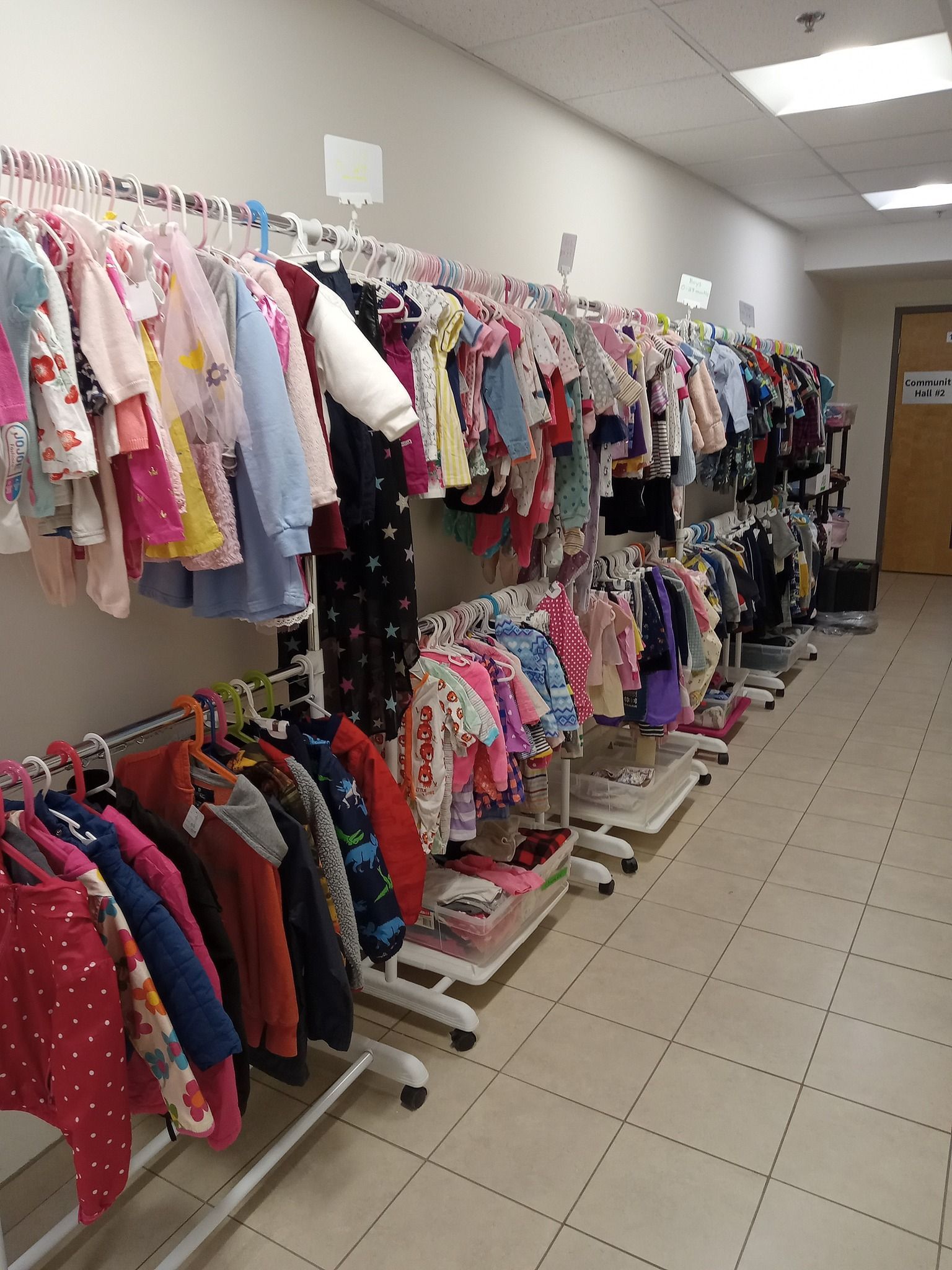 A long hallway with multi-level clothing racks. Children's clothes are hung neatly down the entire hallway.