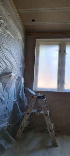 Renovatiekamer met met plastic beklede wand, trapladder en licht raam.