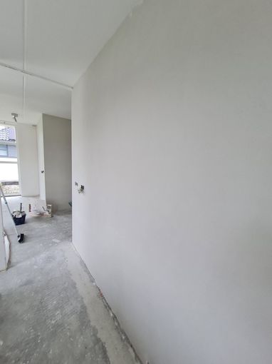 Onafgewerkte witte gang met kale vloer en bouwmaterialen aan de linkerkant.
