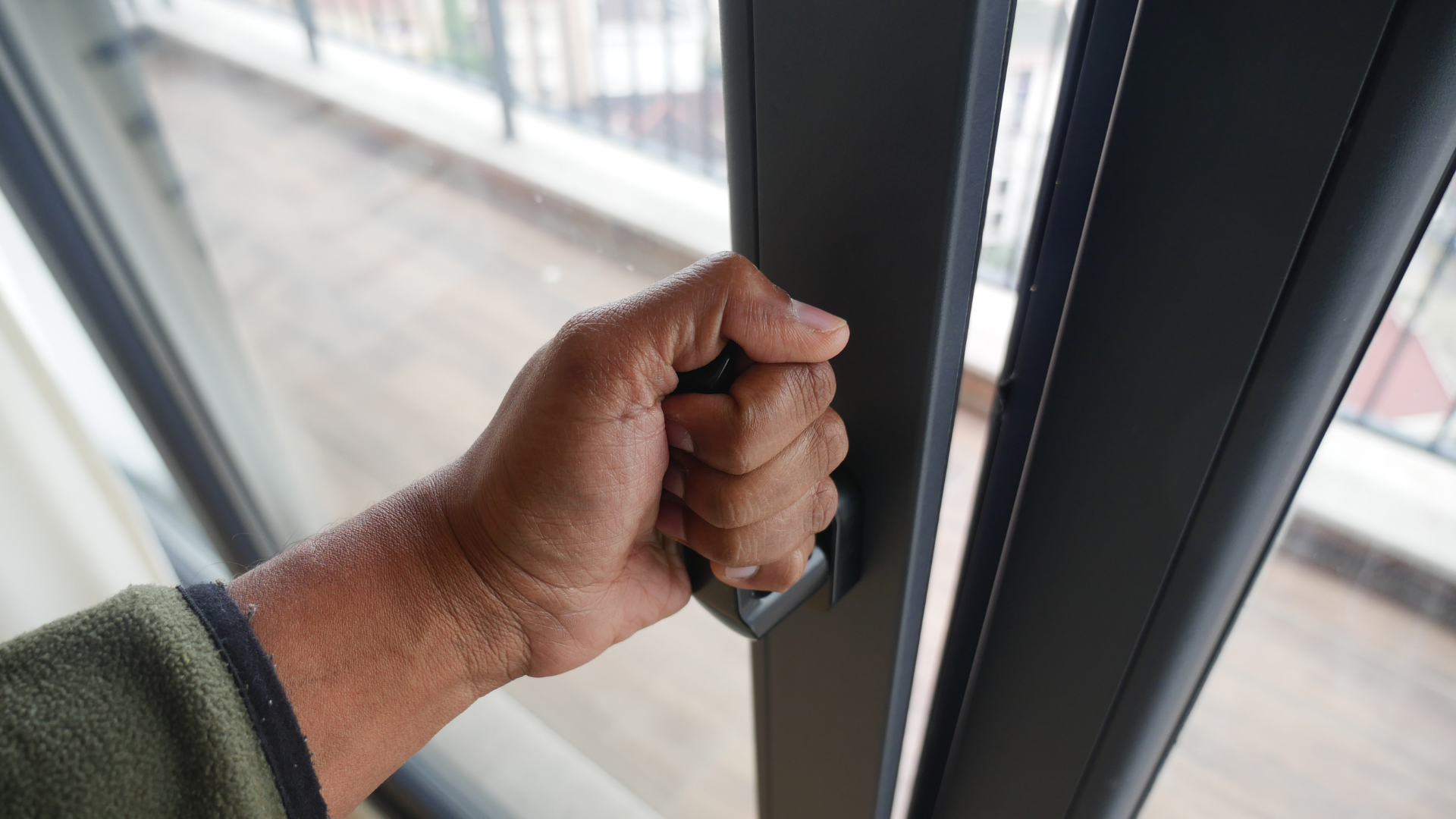 A hand gripping the handle of a dark metal sliding door frame to open it.