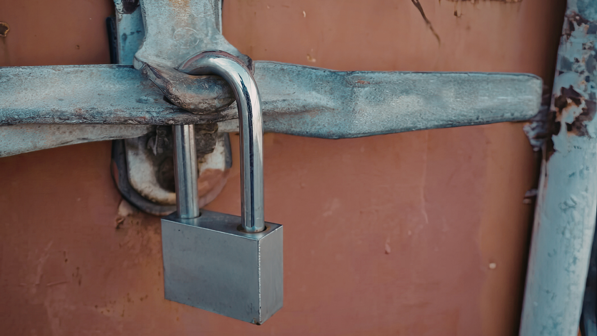 A silver padlock secured on a metal latch against a rusted, reddish-brown door.
