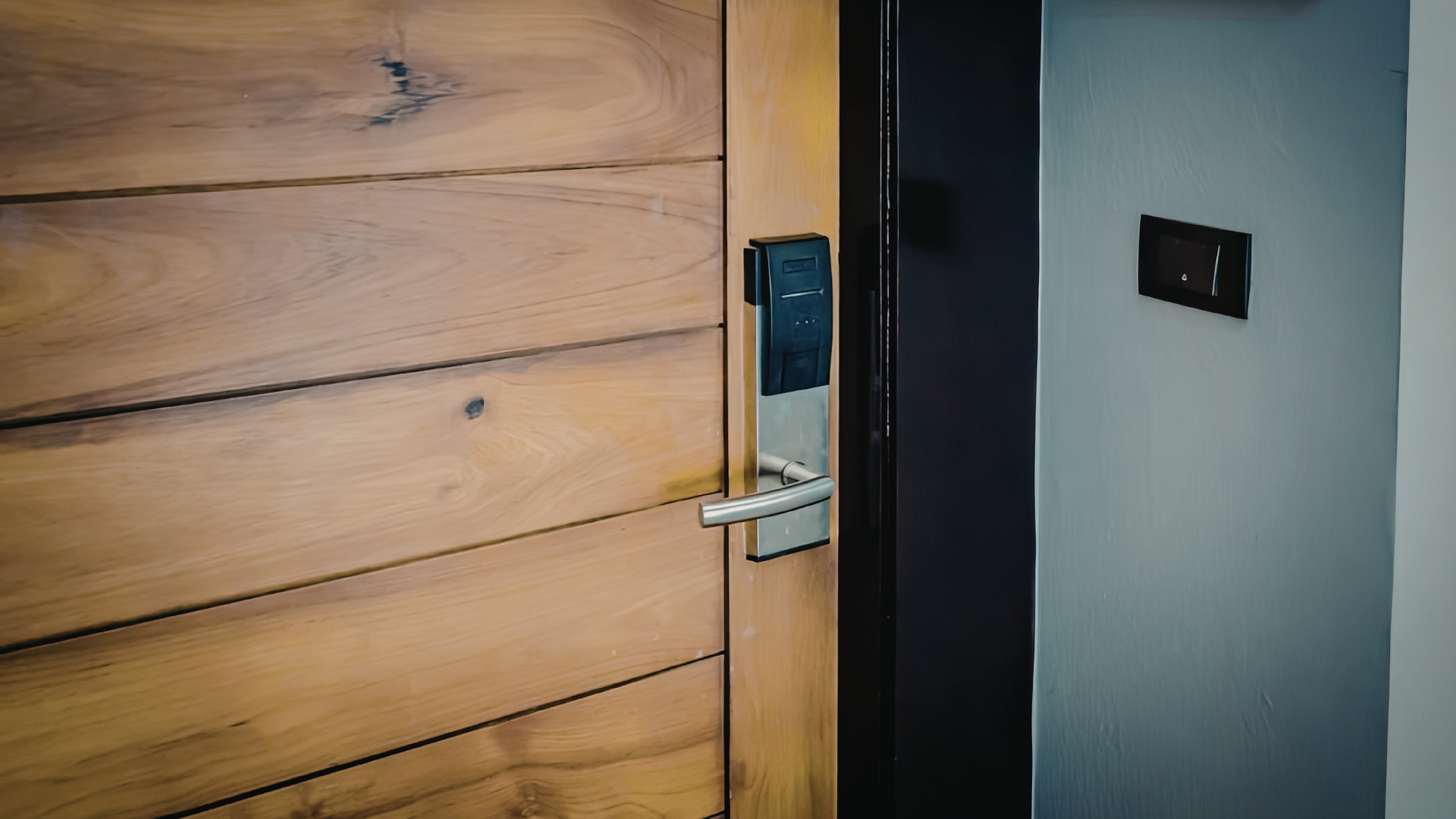 A close-up of a wooden door featuring a modern, metallic electronic smart lock with a lever handle.