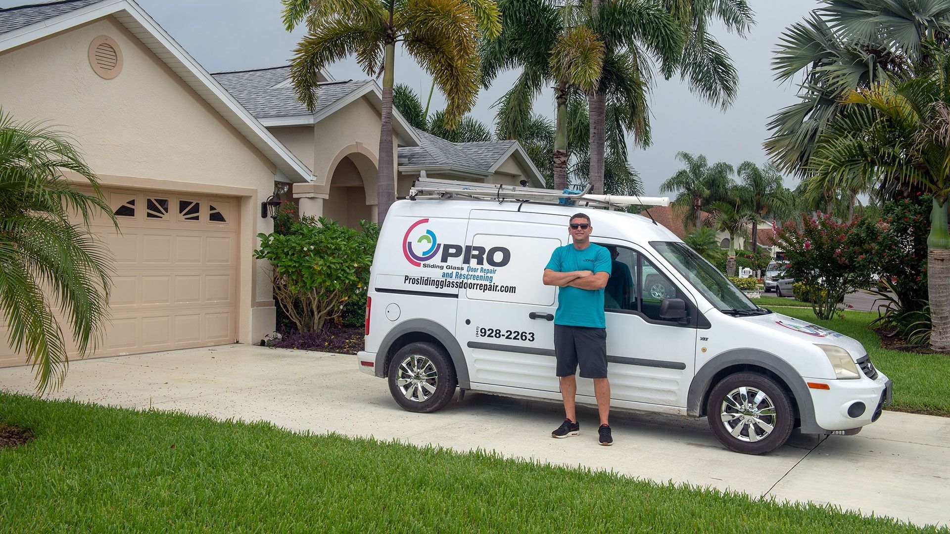 A person in a blue shirt stands next to a white service van parked in a residential driveway with palm trees.