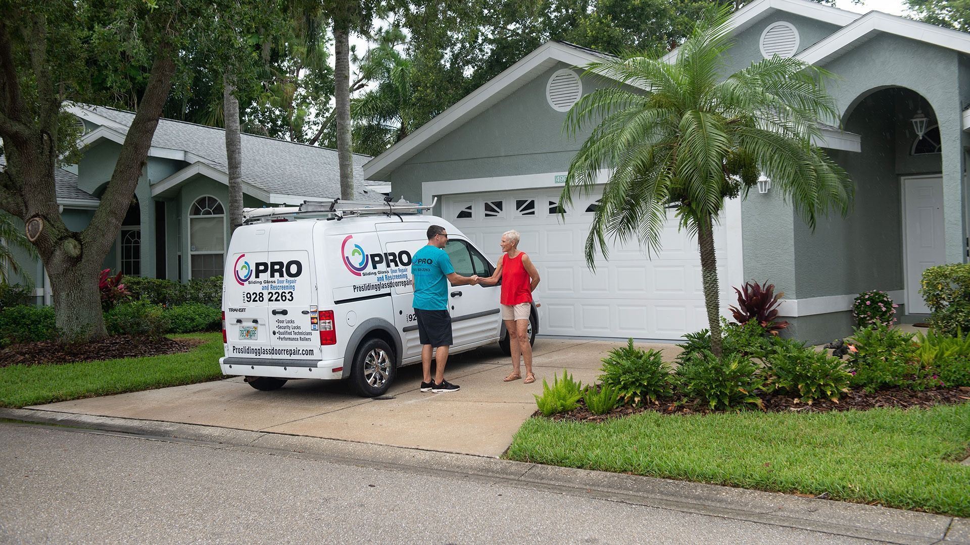 A person in a Pro-Tec branded shirt shakes hands with a resident in their driveway next to a white service van.